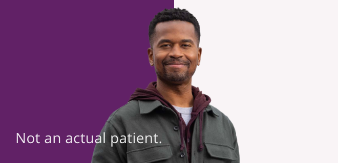 A young Black man standing looking forward and smiling. Not an actual patient.